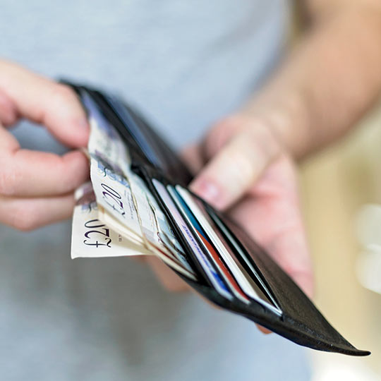 Hands holding a black wallet full of credit cards and twenty pound notes