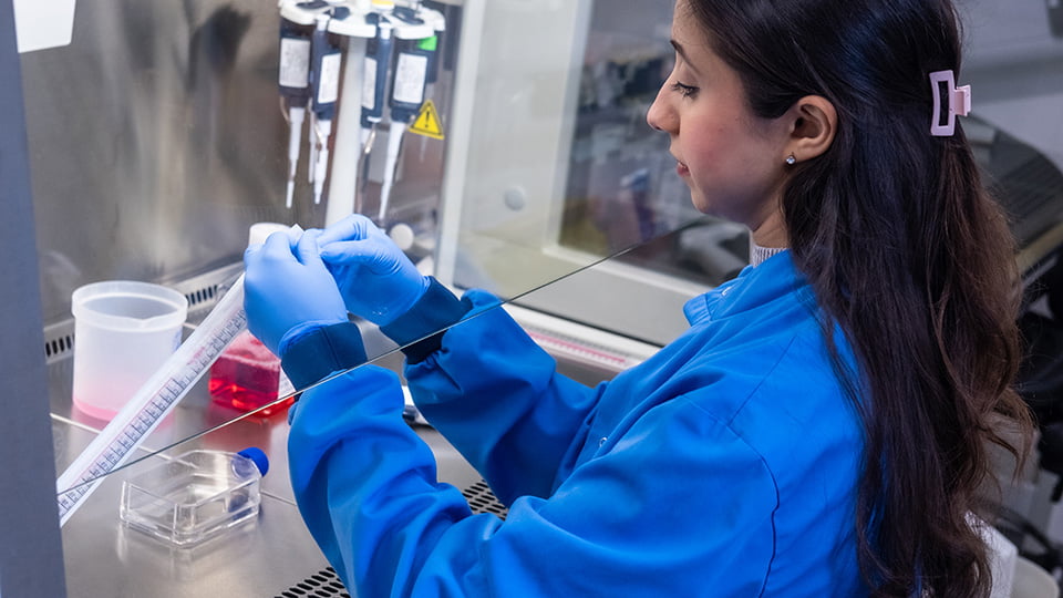 A postgraduate sports science student wearing a blue lab coat carrying out an experiment in a fume cupboard