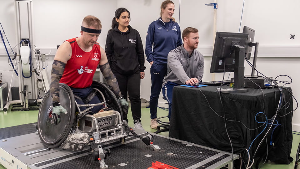 A wheelchair athlete on a treadmill being monitored by three researchers looking at a computer screen