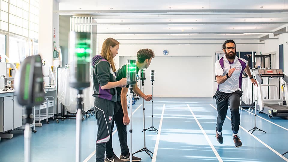 A male runner in a lab being monitored with lasers by two sports science students