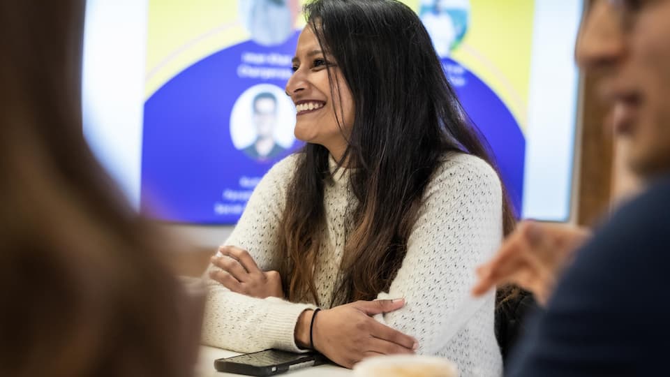 A student smiling with their arms folded on a table