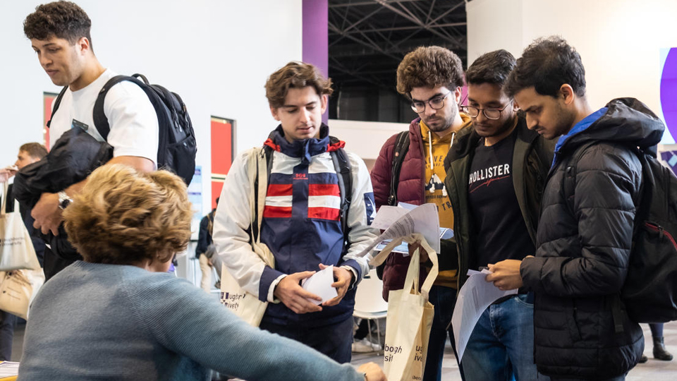 A group of students gather at a stand to speak with a member of staff