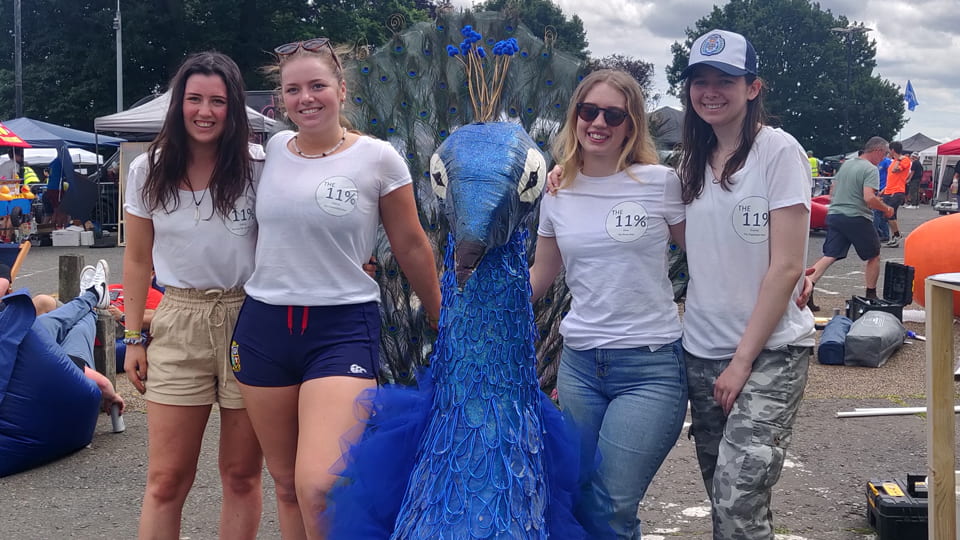 Four students standing with a blue peacock structure