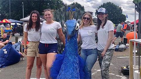 Four students standing with a blue peacock structure