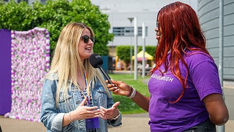 Two people. A student holds a microphone whilst Amy Ward speaks.