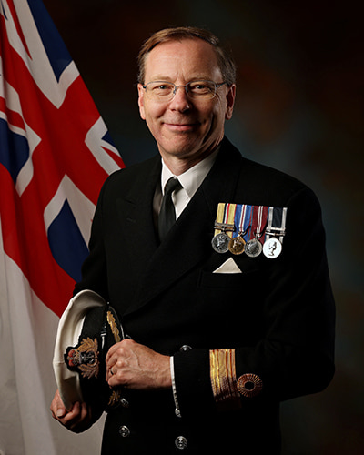 Commodore Dave Joyce wearing uniform and holding a hat. There are medals on his chest.
