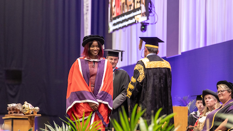 Ama smiling wearing a cap and gown. There is a person standing behind her. Lord Coe faces Ama.