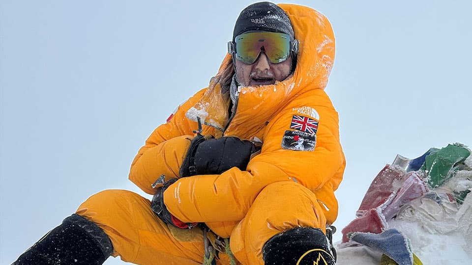 Michal is sitting in a snowsuit on top of Mount Everest.