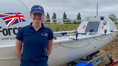 Zara is smiling and standing in front of a boat. She is wearing a navy hat and t-shirt with the Team Forces logo on them.