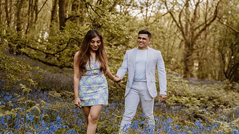Aditya Mukherjee and Aarushi Mittal walking through the bluebells at Burleigh Wood, Loughborough University. They are walking holding hands and smiling together.
