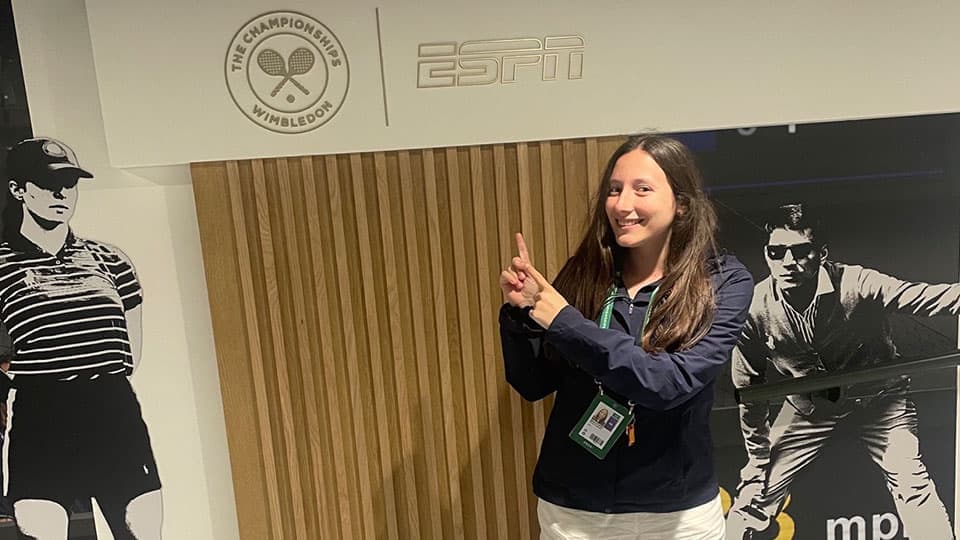 Bethan is standing pointing at a sign that says 'ESPN' and she is smiling.