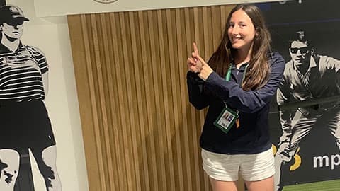 Bethan is standing pointing at a sign that says 'ESPN' and she is smiling.