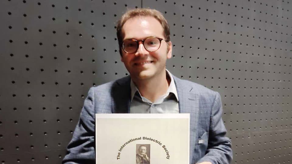 Stavros holding The Debye Prize 2024 and smiling against a plain background.