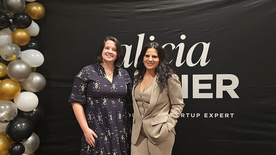 Alicia Soulier, CEO of SalonScale standing with Founder of CEO Stories Media with a black background and some gold, white, black and silver balloons to the left.