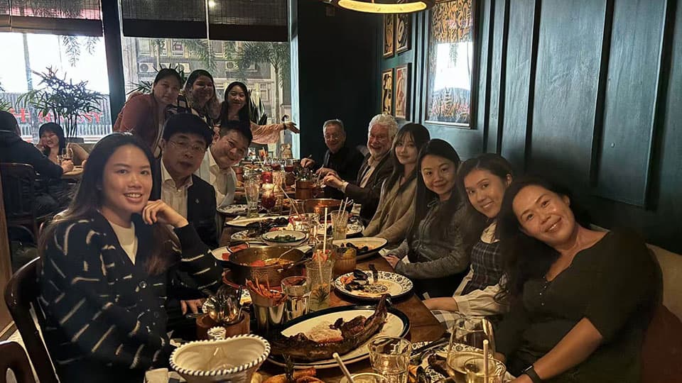 A group of twelve alumni at Loughborough University's mixer event in Hong Kong on 19th November. They are sat smiling and talking to each other with food and drinks in front of them at a table.
