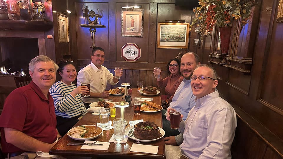 A group of six alumni sitting down with drinks and a meal in front of them at a table at Loughborough University's alumni event on 13 November 2024.