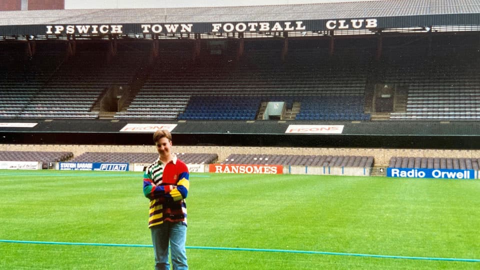Giles is standing on the pitch at Ipswich Town Football Club