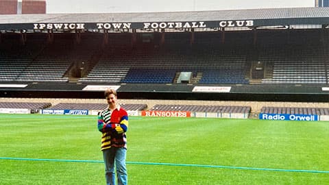 Giles is standing on the pitch at Ipswich Town Football Club