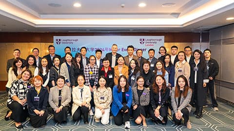 A group of alumni in Shanghai at Loughborough University's event on 14th November 2024. The group are in front of a screen for a presentation which has Loughborough University's logo on it.
