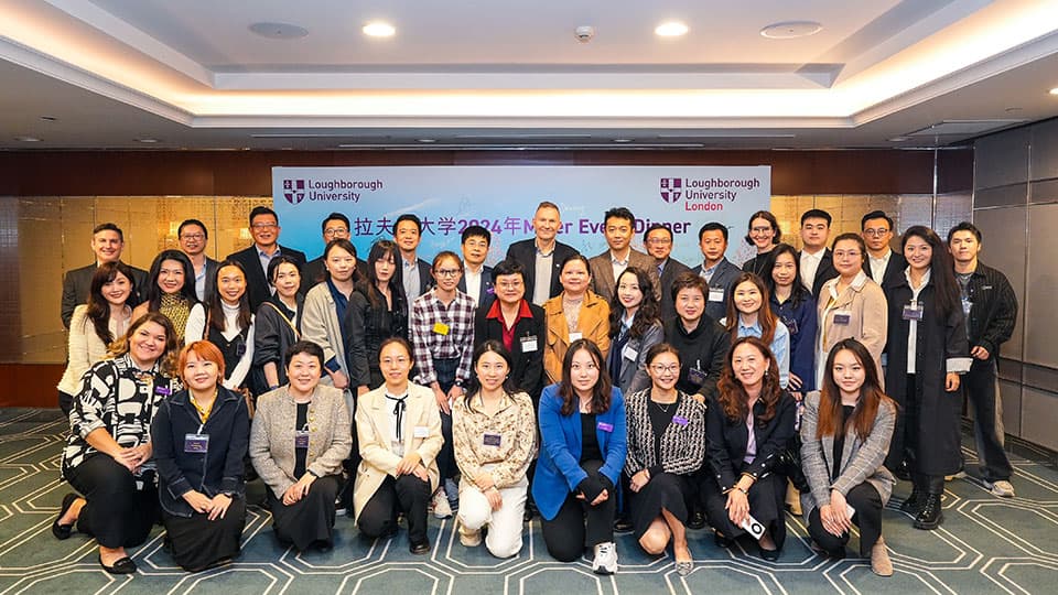 A group of alumni in Shanghai at Loughborough University's event on 14th November 2024. The group are in front of a screen for a presentation which has Loughborough University's logo on it.
