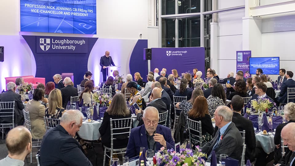 The Vice-Chancellor stands on stage in front of a room of seated guests