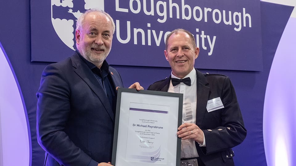 Professor Nick Jennings hands Dr Michael Peyrebrune a certificate. They stand together in front of a Loughborough University banner.
