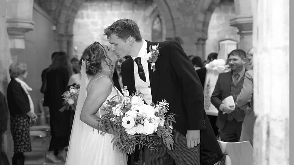 Tom and Sophie kissing in a church surrounded by friends and family in the background.