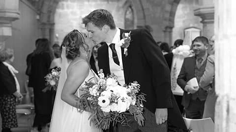 Tom and Sophie kissing in a church surrounded by friends and family in the background.