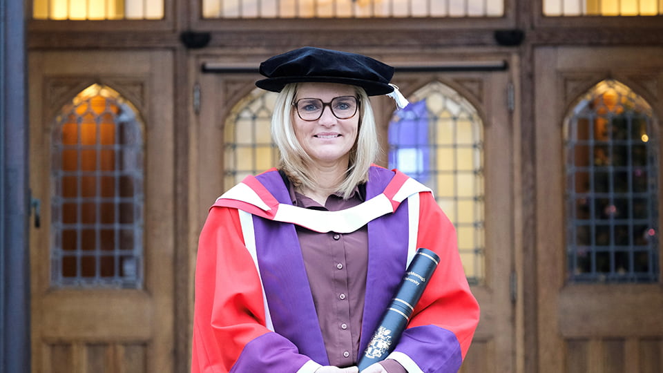 Sarina Wiegman standing at the front of the Hazlerigg Building wearing a graduation cap and red gown