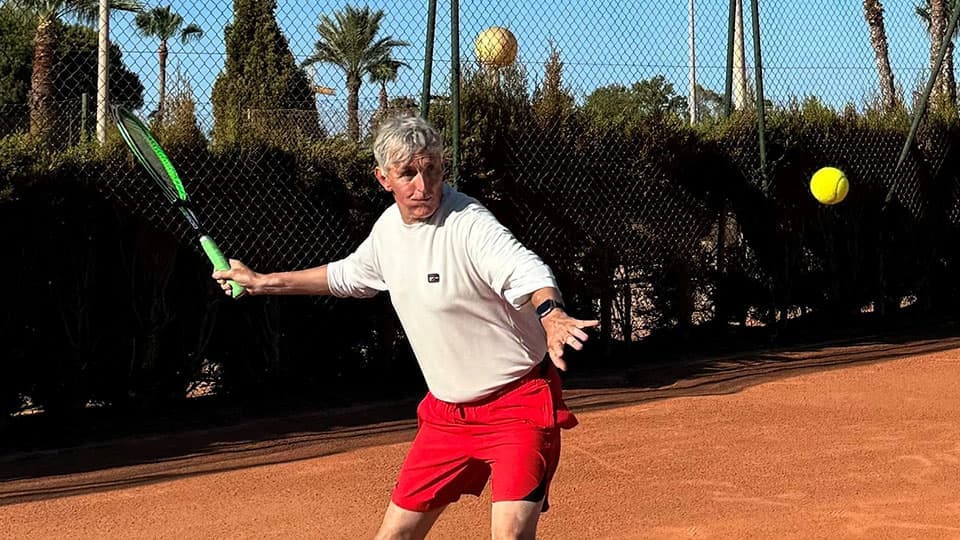 Paul Obey playing tennis on holiday in Spain (at La Manga). The tennis bat is mid swing as he is going to hit the ball.