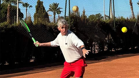 Paul Obey playing tennis on holiday in Spain (at La Manga). The tennis bat is mid swing as he is going to hit the ball.