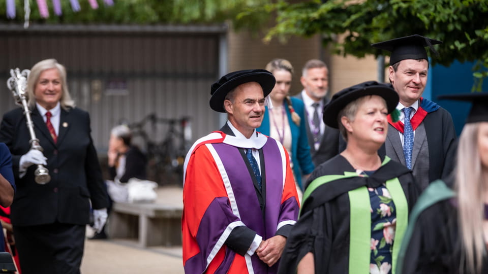 Sir Warren East FRS FREng processing wearing a red gown alongside other people in gowns for graduation.