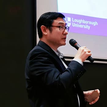 A headshot of Charles Li standing up speaking and he is holding a microphone.