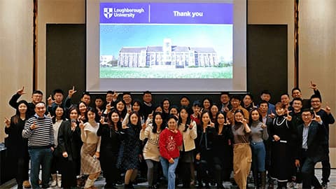 A group of alumni at an end-of-year event in front of a presentation with the Loughborough University logo on it in Beijing.