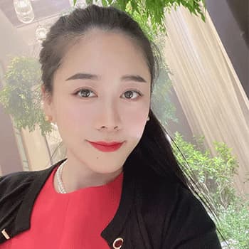 A close up of Sabrina. She is wearing a black cardigan, red top and red toned lipstick. She has her hair tied in a ponytail and is smiling at the camera.