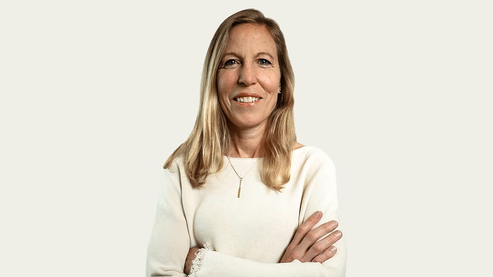 A headshot of Sarah Massey. She is wearing a white jumper and is standing against a white background with her arms folded and she is looking at the camera.