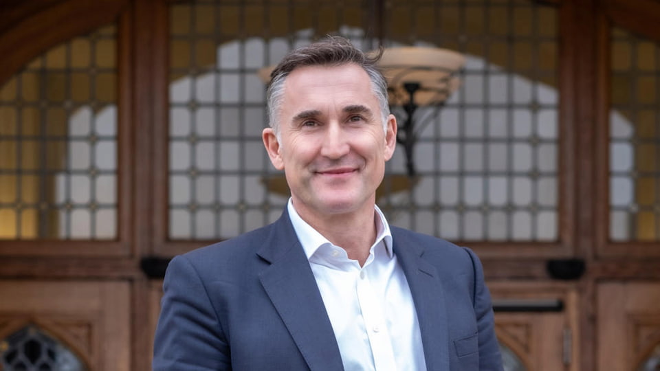 Steve Varley in a shirt and suit jacket smiling outside the entrance to the Hazlerigg Building