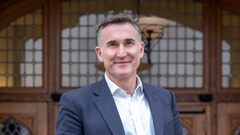 Steve Varley in a shirt and suit jacket smiling outside the entrance to the Hazlerigg Building