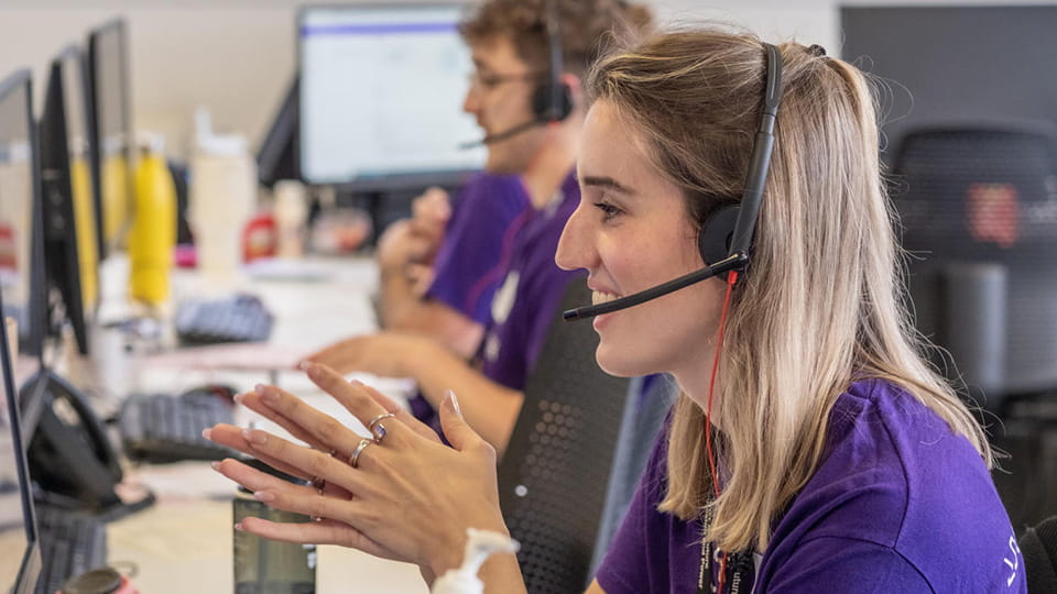 A call handler wearing a headset and purple tee-shirt talks on the phone to an applicant