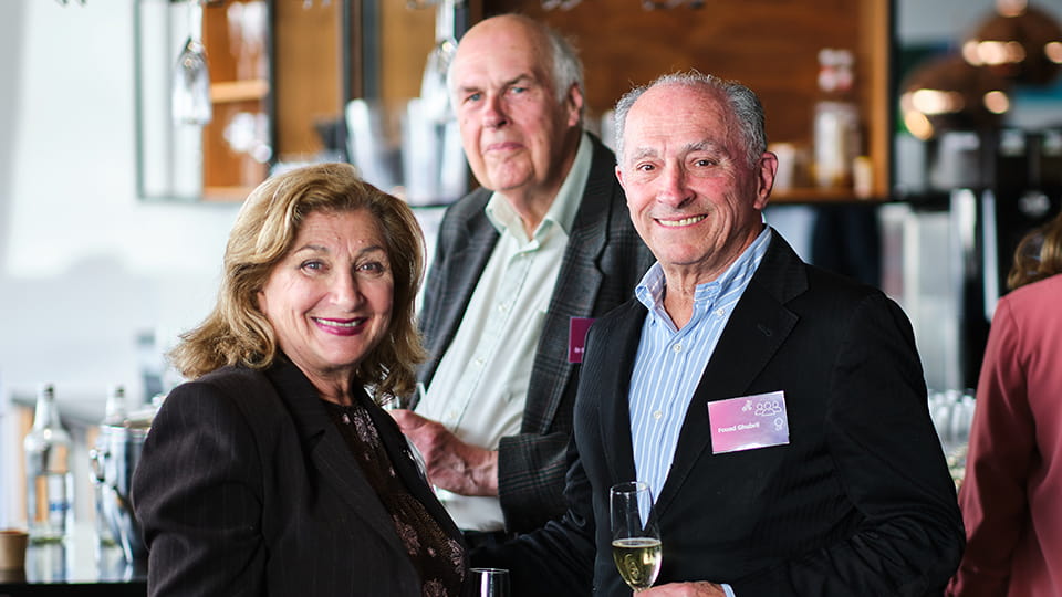 Three people standing facing towards the camera, smiling. In the background is a bar.