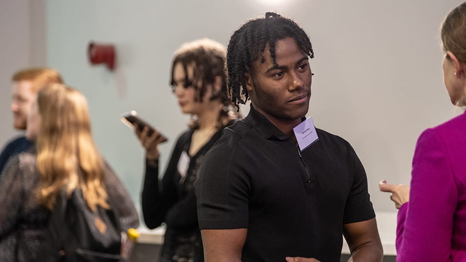 A student looking at another person. Other students are in the background.