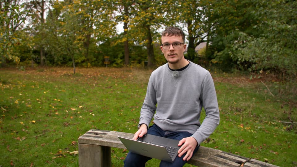 Student Rory on a bench outside with a laptop