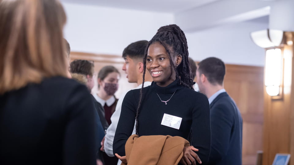 A student scholar is smiling at someone. There are people in the background.
