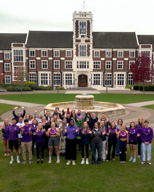 A group of people waving outside Hazlerigg Building