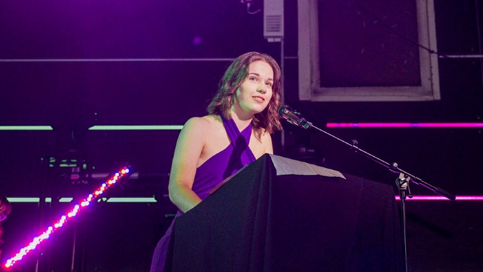 Daisy Newton standing on stage speaking into a microphone.