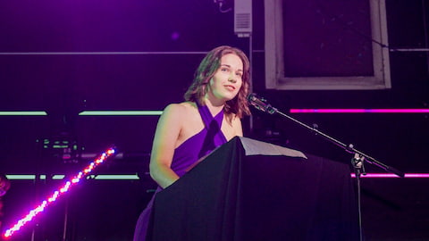 Daisy Newton standing on stage speaking into a microphone.