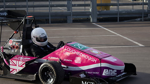 A driver in the LUMotorsport car in a car park. The car is predominantly pink and has a variety of logos on it.