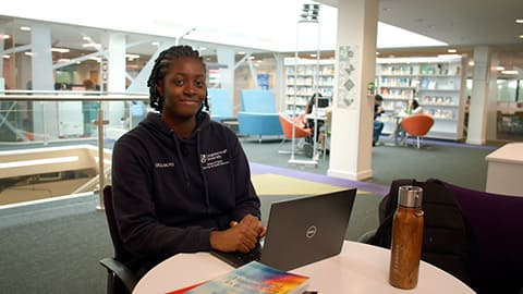 Student, Joy, is seated in the library, smiling