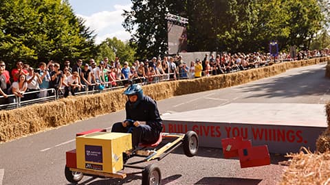 Team Tetra’s Soapbox car driven by a student. There are people at the side of the racetrack watching.