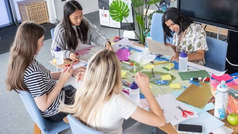 A group of students sat around a table working together with different coloured bits of paper and card